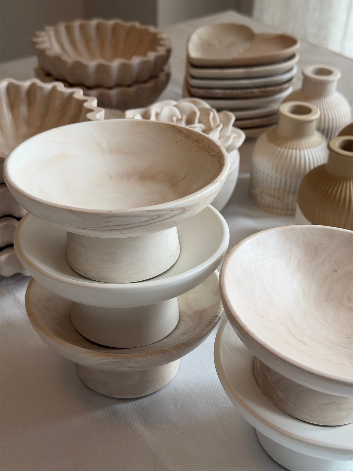 This image shows a small set of Mooch bestsellers on a soft, neutral surface, including Jesmonite bowls, trays, and a candle in calm, muted tones, arranged simply and uncluttered for a clean, focused look.