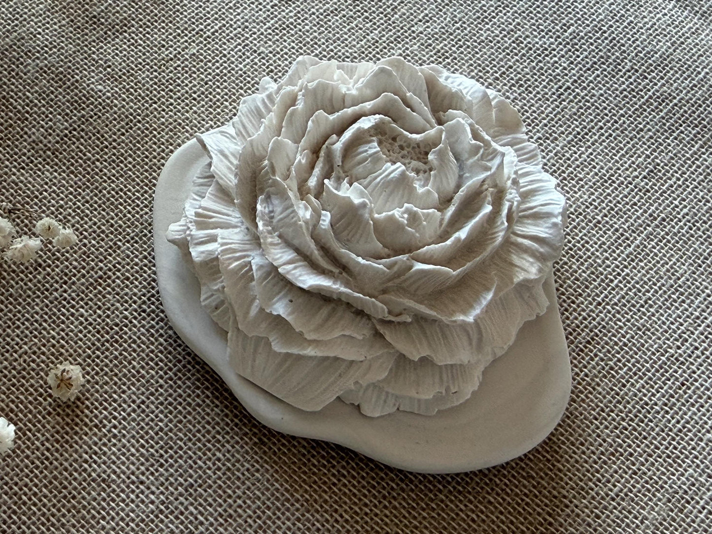 White ceramic flower and pebble on a textured beige surface